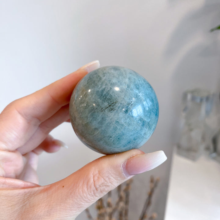 Hand holding a blue-green crystal ball against a neutral background