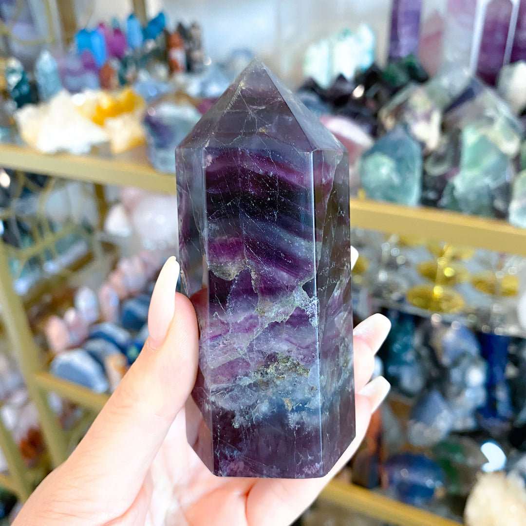 Hand holding a purple crystal tower in a store with various crystals in the background