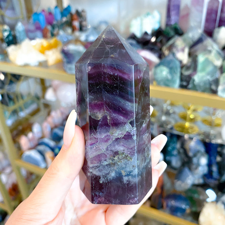 Hand holding a purple crystal tower in a store with various crystals in the background