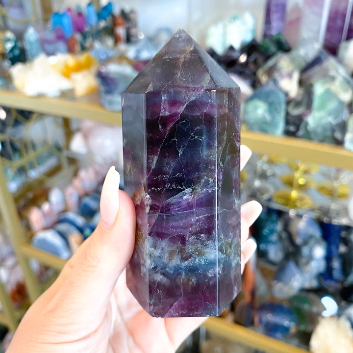 Person holding a purple crystal in a store with various crystals in the background