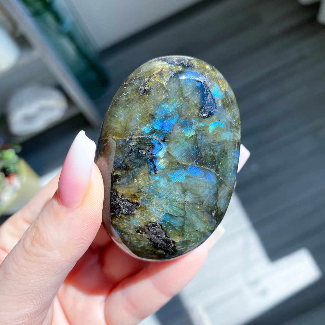 Hand holding a labradorite stone with blue and green patterns