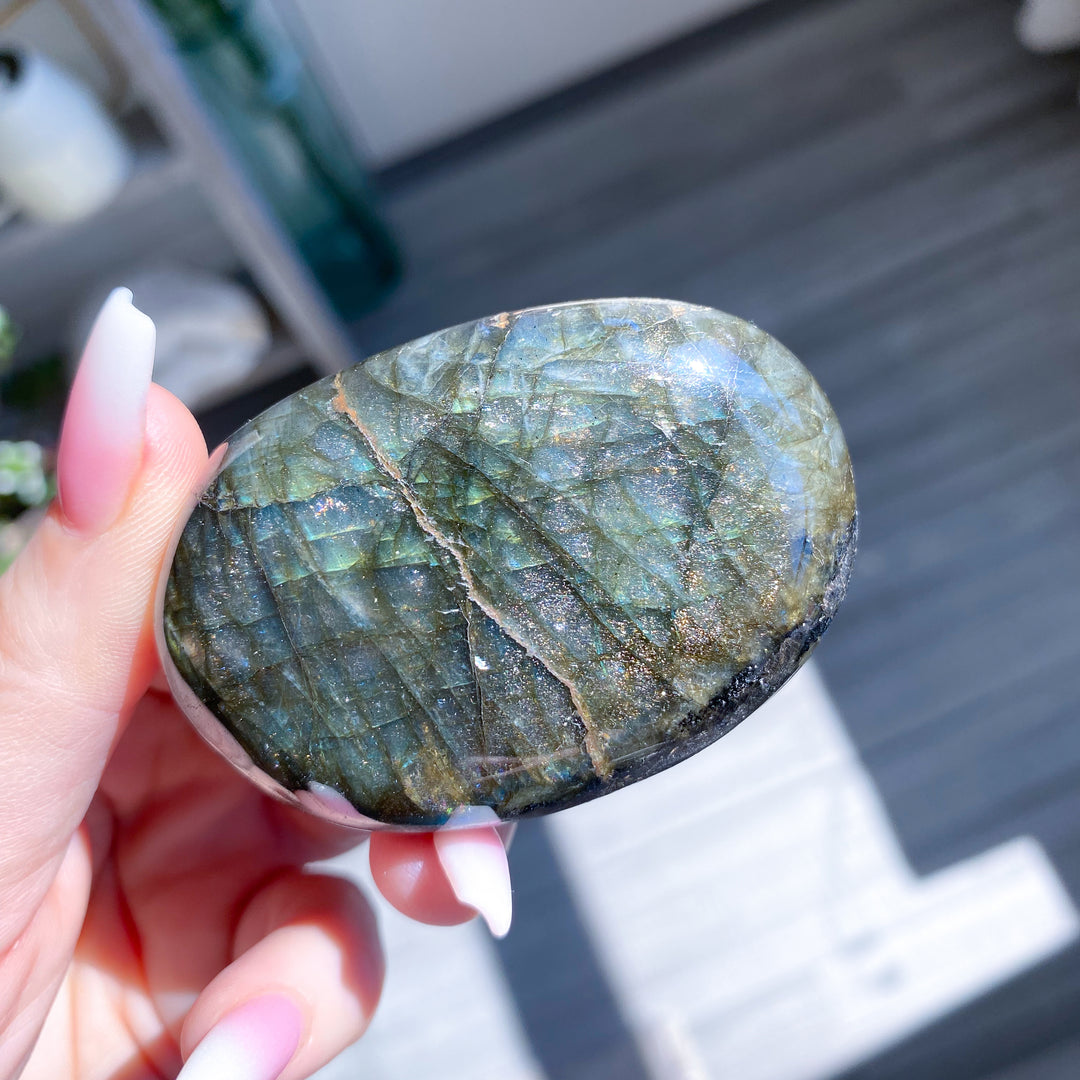 Hand holding a polished labradorite stone outdoors
