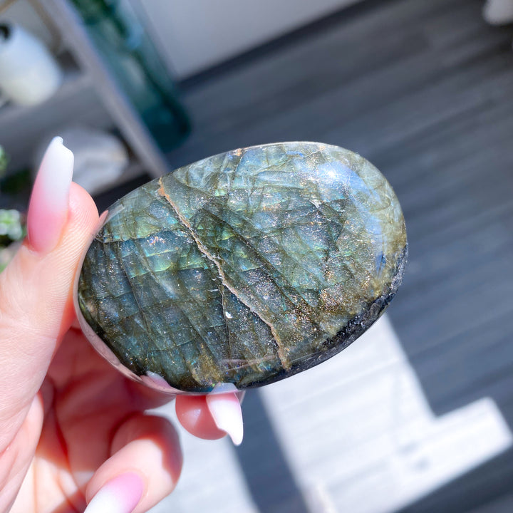 Hand holding a polished labradorite stone outdoors
