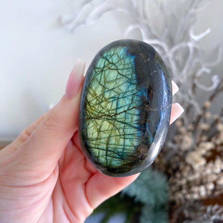 Hand holding a labradorite stone with a natural pattern against a blurred background