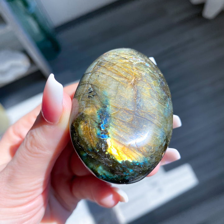Hand holding a labradorite stone with colorful patterns
