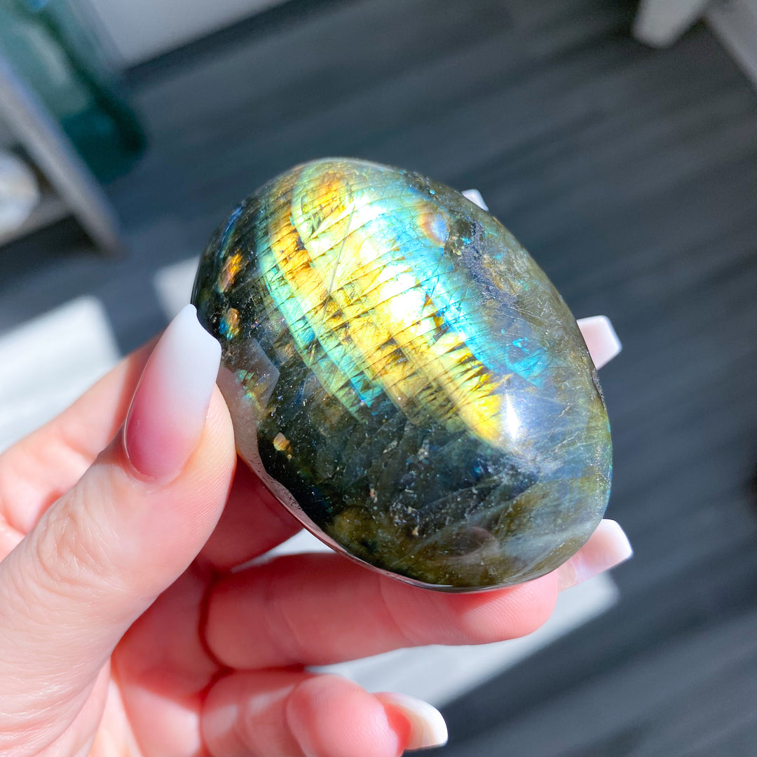 Hand holding a colorful labradorite stone on a blurred outdoor background