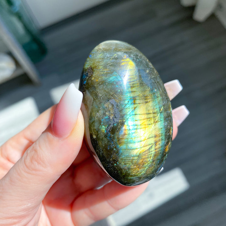 Hand holding a labradorite stone with colorful sheen on a blurred background