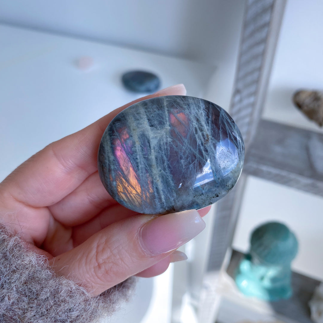 Hand holding a rainbow obsidian stone with a blurred indoor background