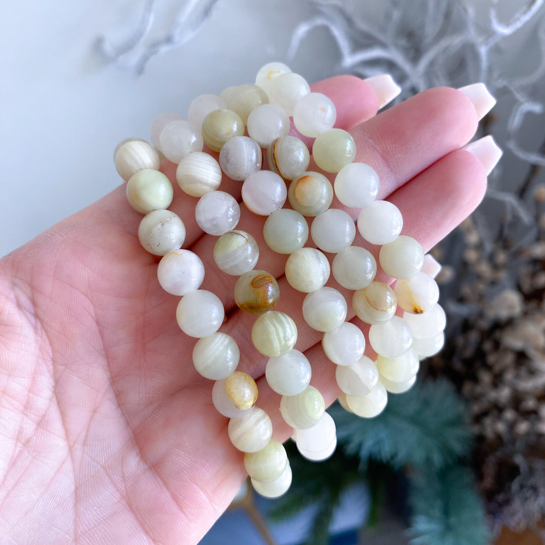 Hand holding a string of light green jade beads against a neutral background