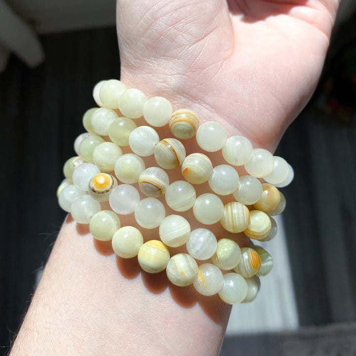Stack of light-colored beaded bracelets on a hand against a neutral background