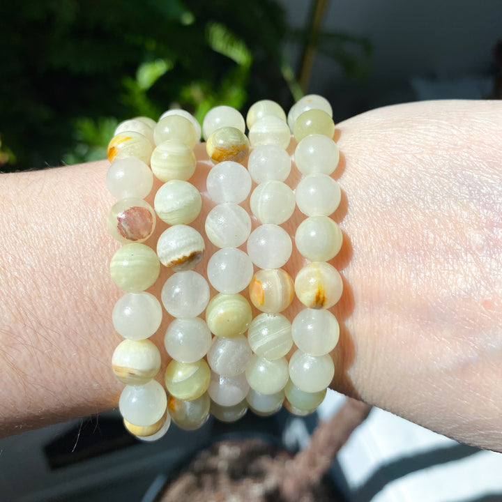 Close-up of a wrist wearing multiple light-colored beaded bracelets with a blurred natural background.