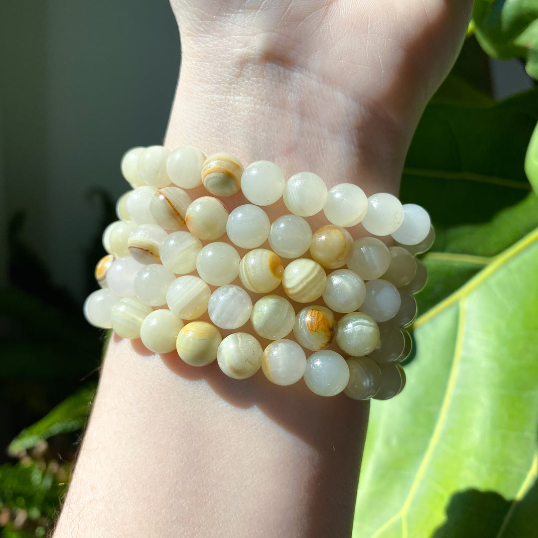 Stack of white and yellow beaded bracelets on a wrist with green leaves in the background