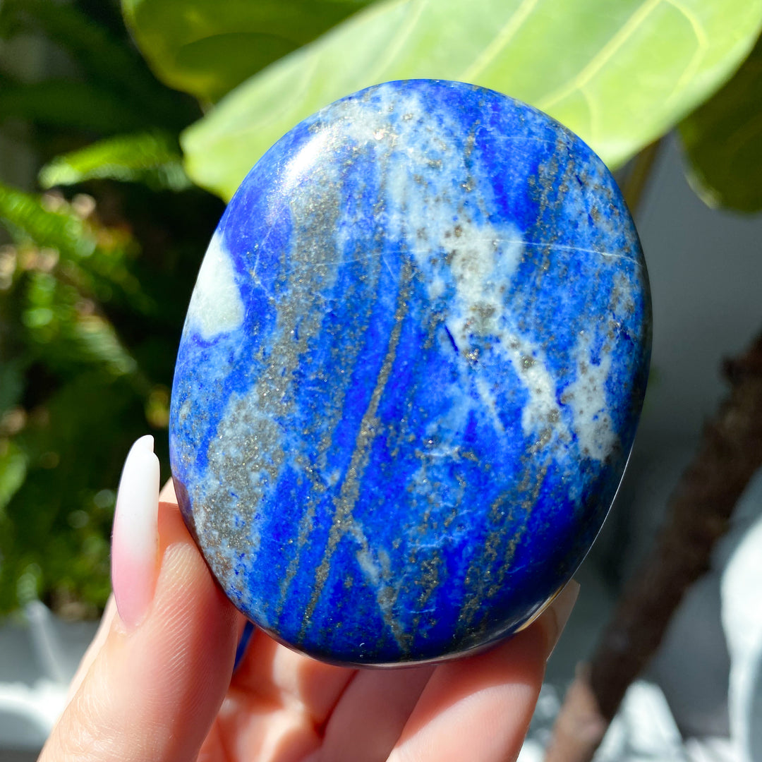 Blue stone held in a hand with a blurred green leafy background