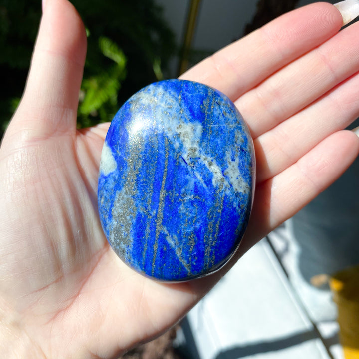 Hand holding a blue and white marbled stone with a blurred outdoor background
