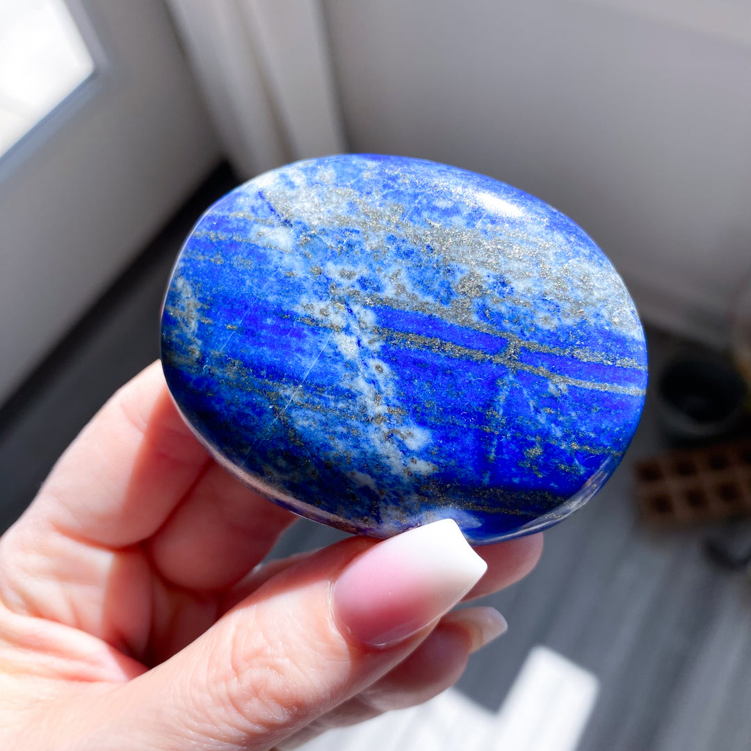 Hand holding a blue stone with patterns, blurred background