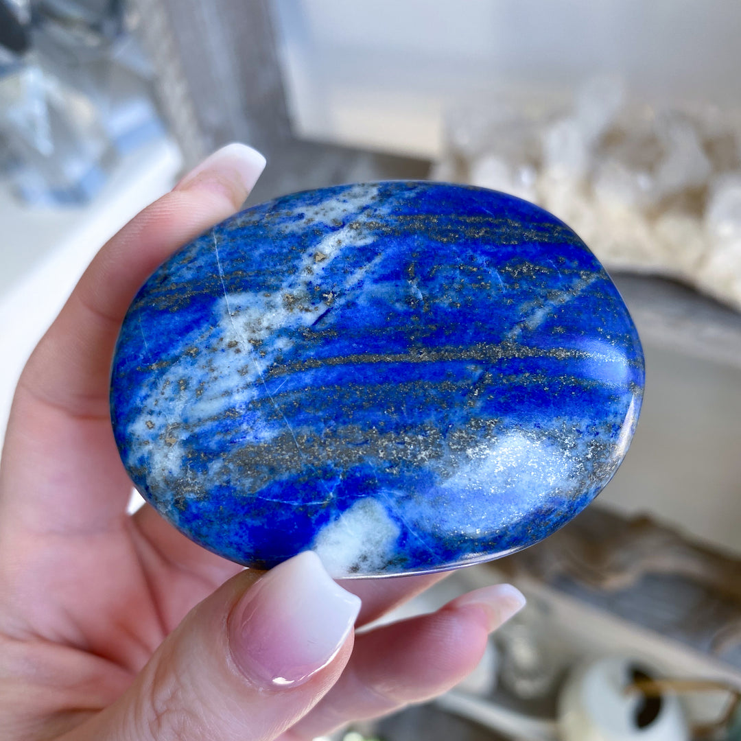 Hand holding a blue stone with white and gray patterns, blurred background