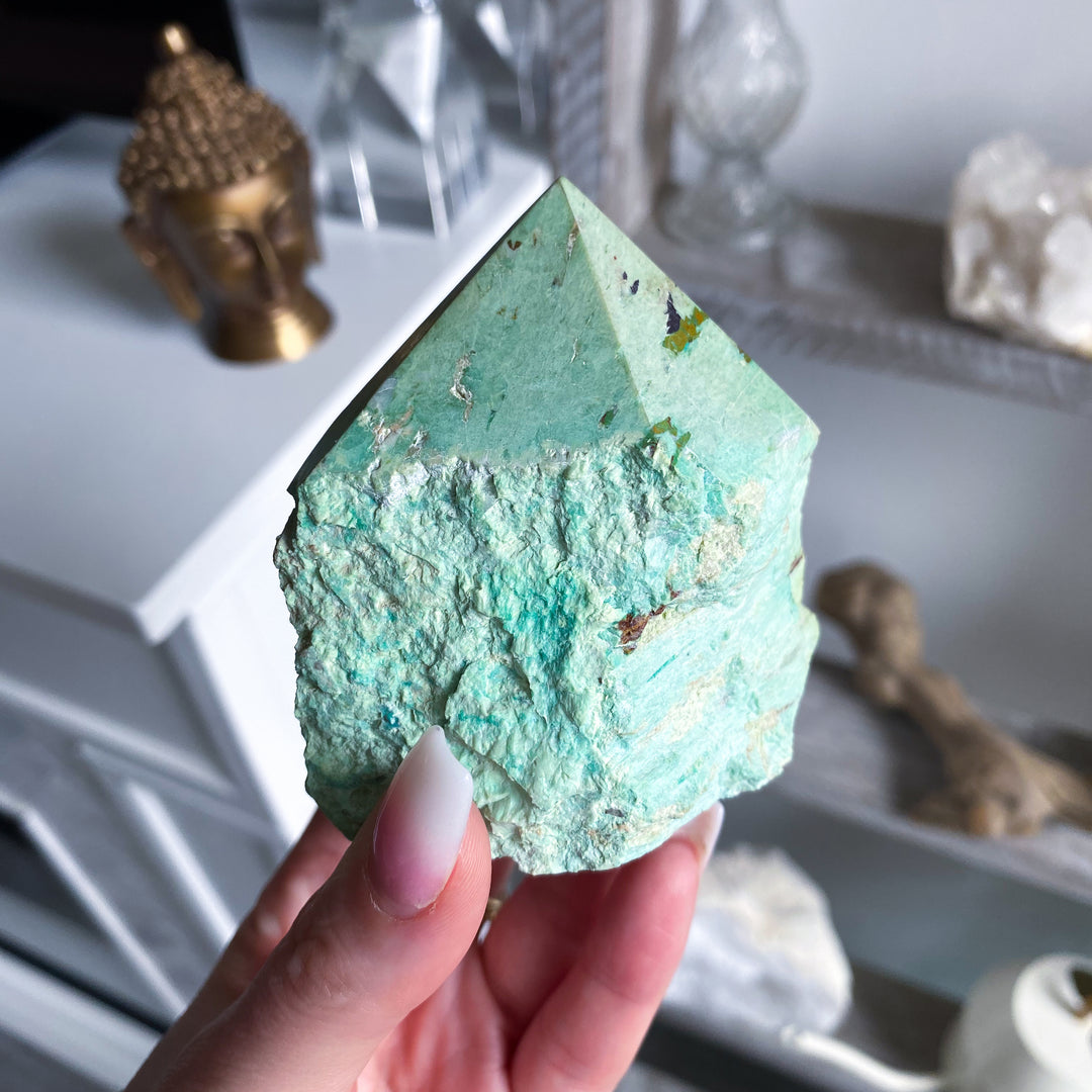 Hand holding a large green crystal with a blurred indoor setting