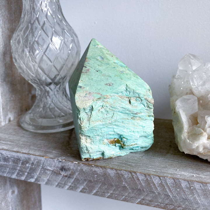 Turquoise crystal on a wooden surface with a glass container and white crystal formation in the background.