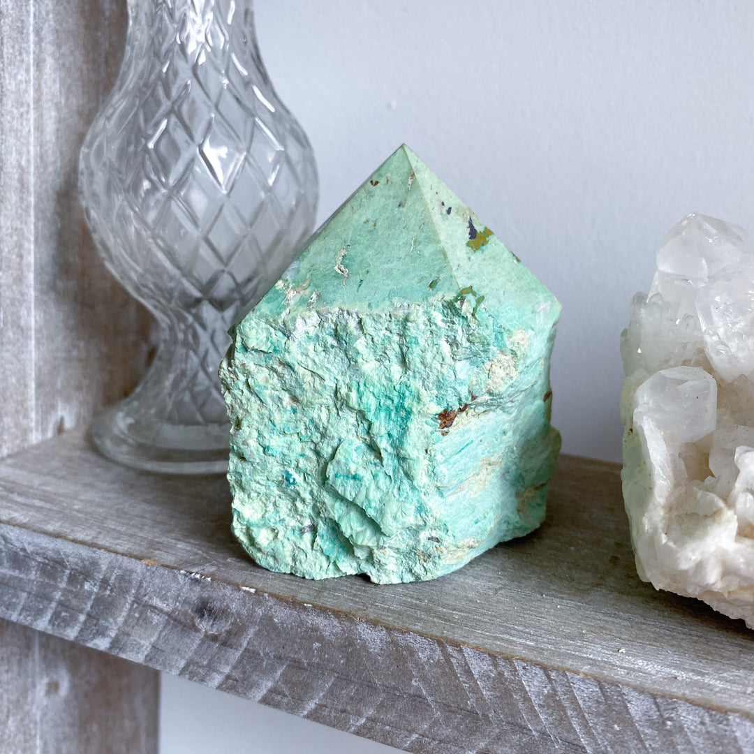 Turquoise crystal on a wooden shelf with a glass container and another crystal in the background.