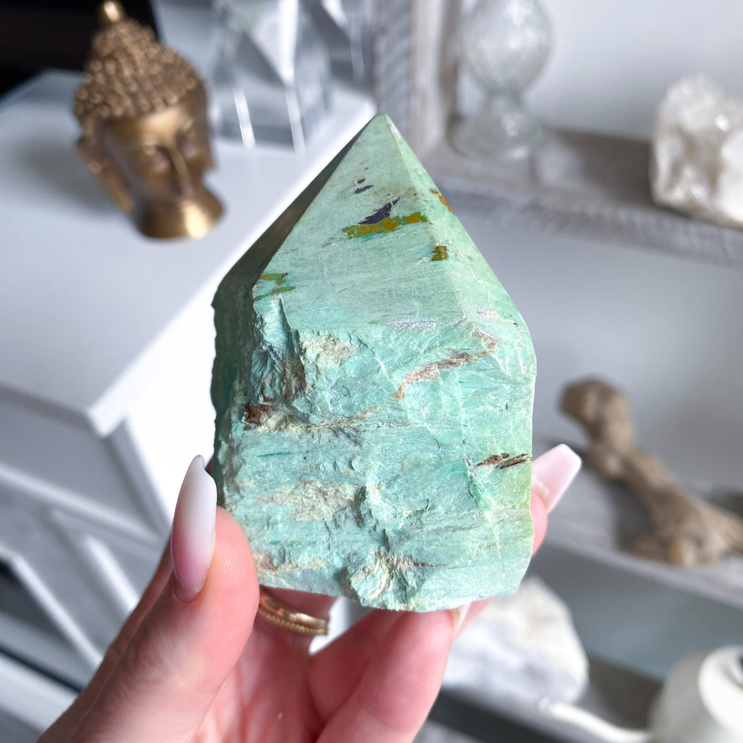 Turquoise crystal held by a hand with blurred decorative background