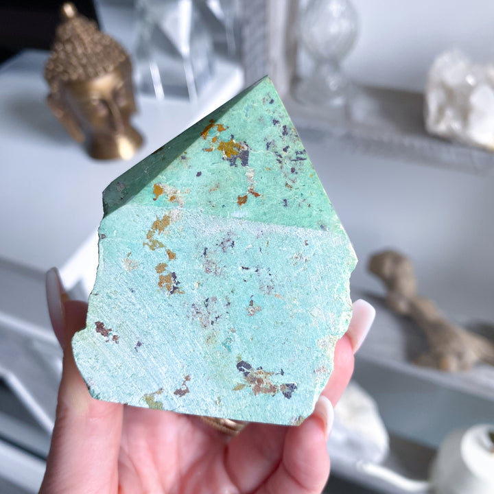 Hand holding a green crystal with embedded stones against a blurred background