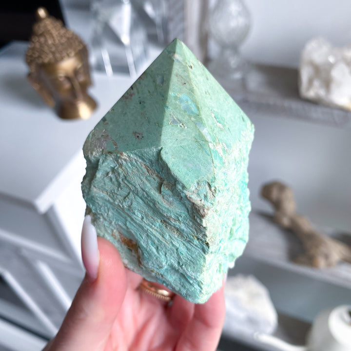 Teal crystal pyramid held by a hand with a blurred background