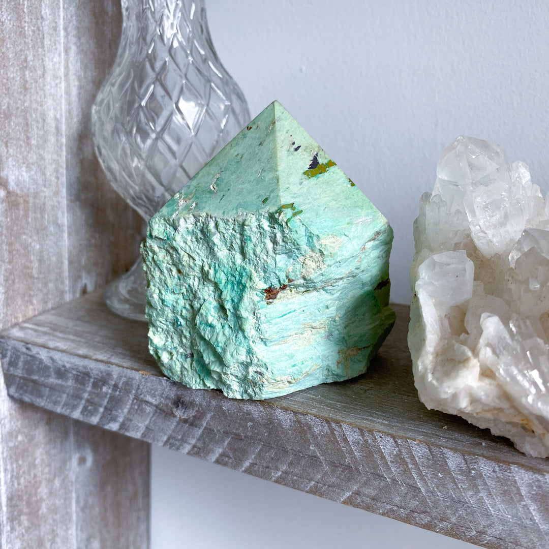Turquoise crystal and white crystal on a wooden shelf with a glass container in the background.