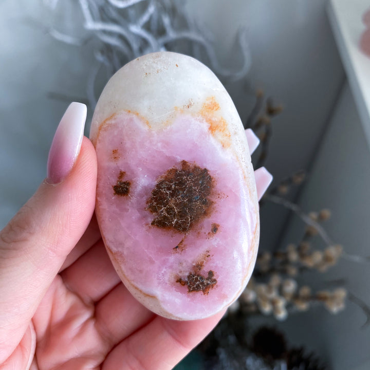 Hand holding a pink and brown geode crystal with a blurred background