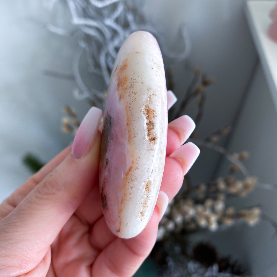 Hand holding a smooth, oval-shaped stone with a blurred natural background