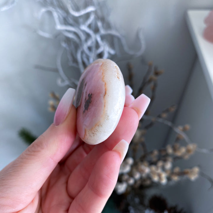Hand holding a small, round, multicolored stone with a blurred natural background