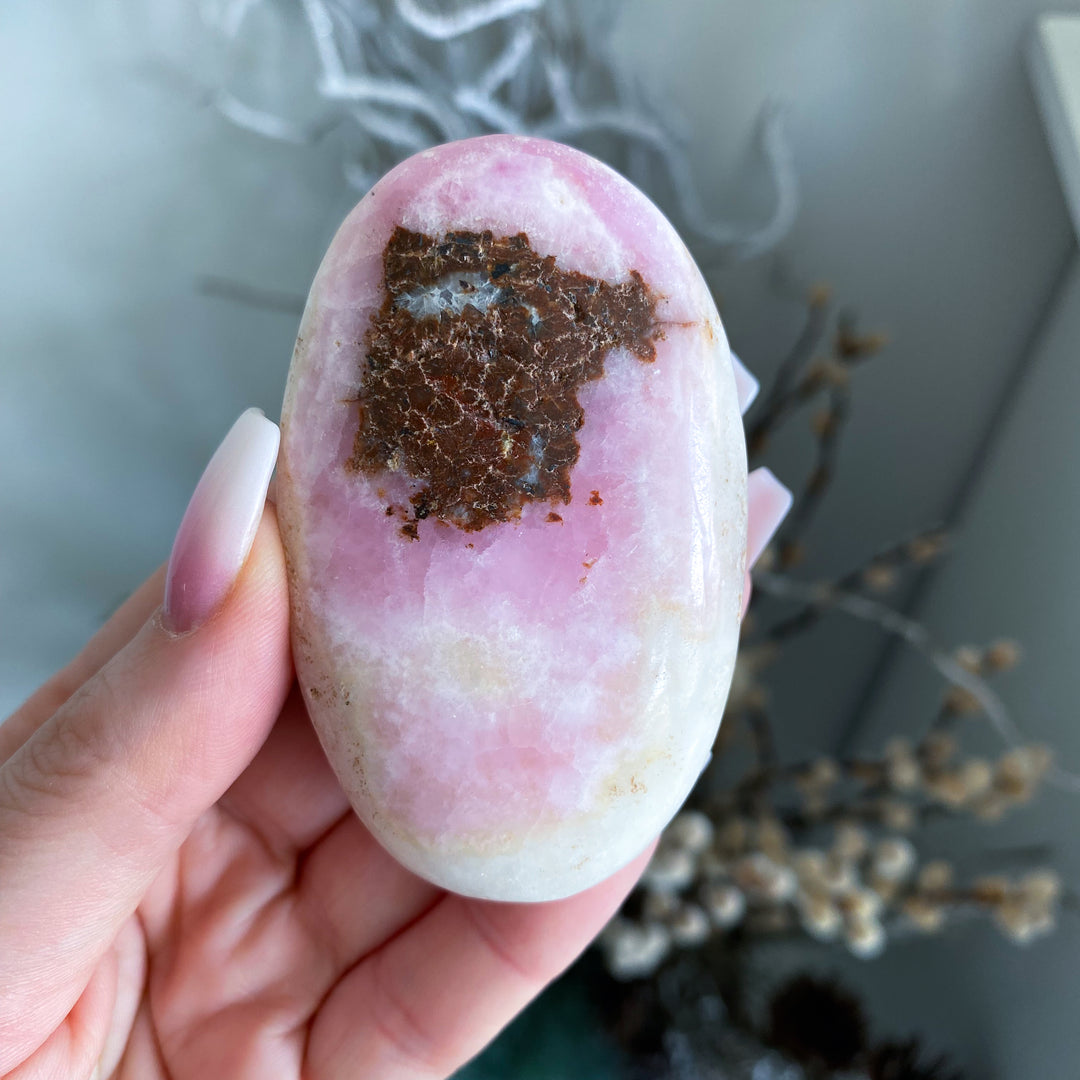 Hand holding a pink and white stone with a brown patch against a blurred natural background