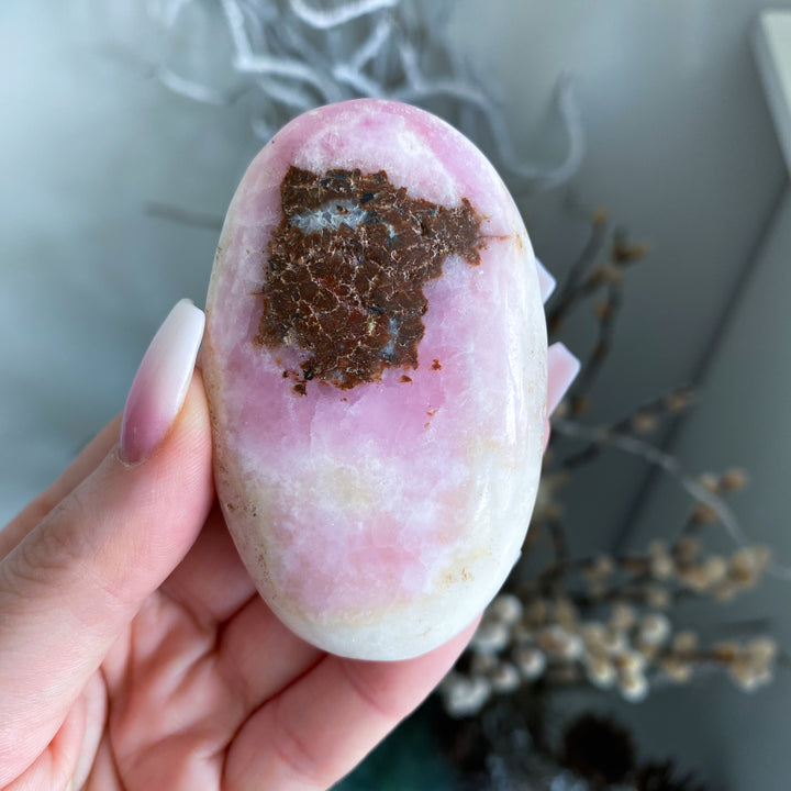 Hand holding a pink and white stone with a brown patch against a blurred natural background