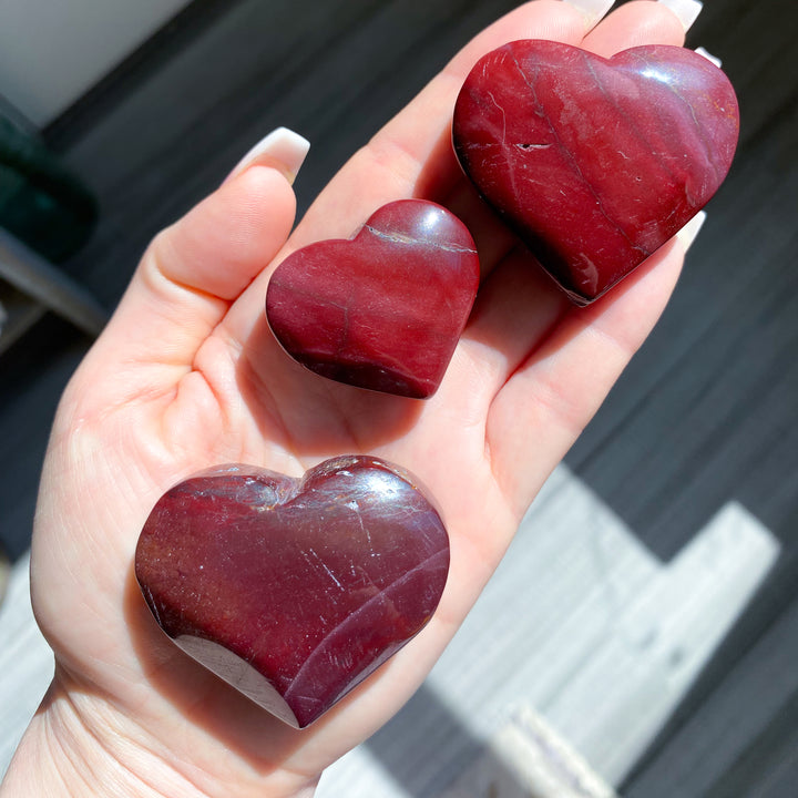 Three red heart-shaped stones held in a hand with a blurred background