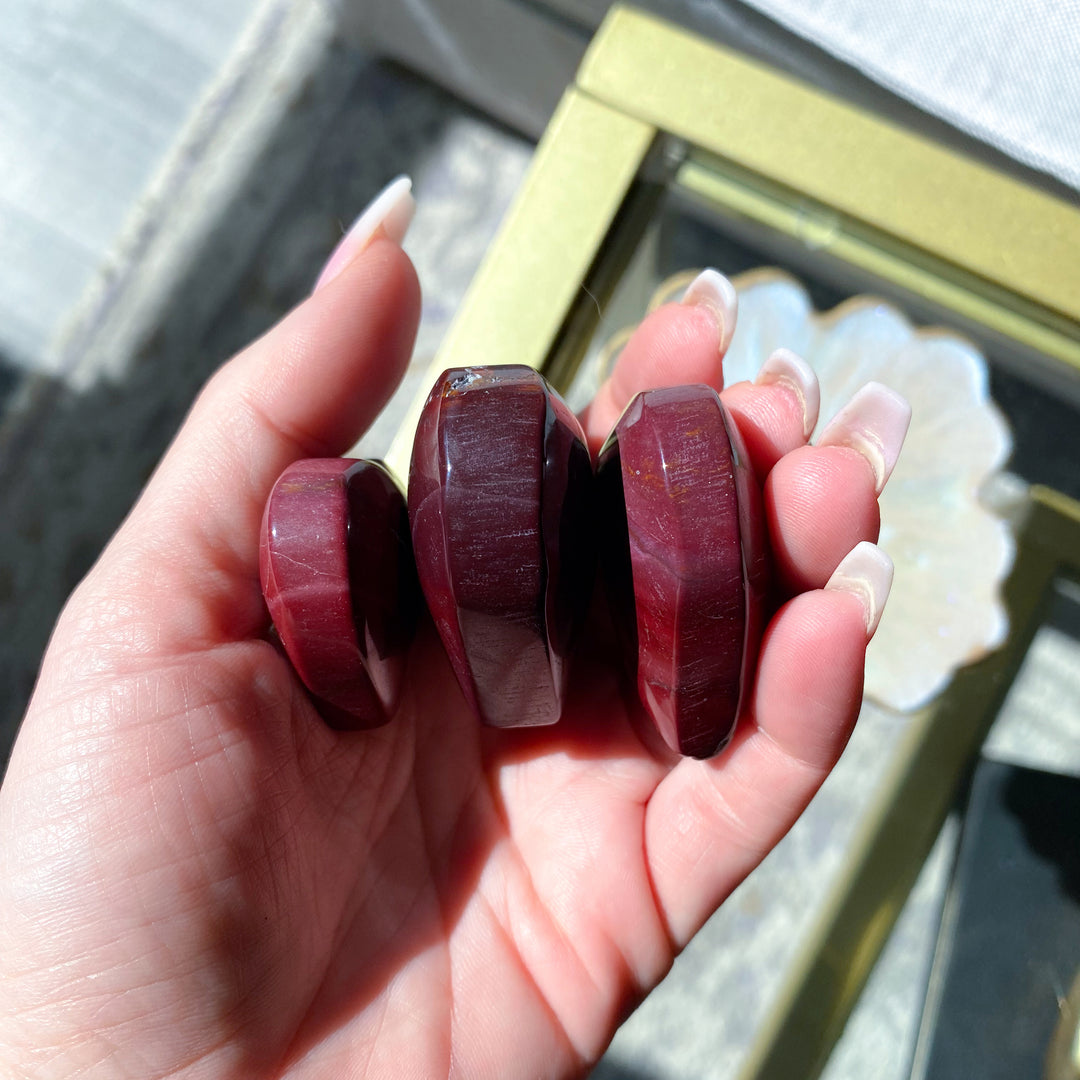 Hand holding three red stone beads with a blurred background