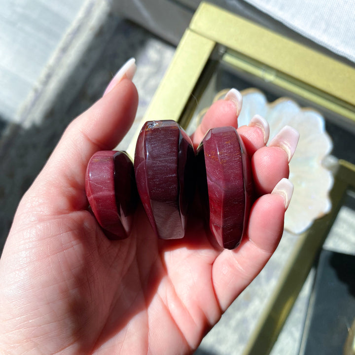 Hand holding three red stone beads with a blurred background