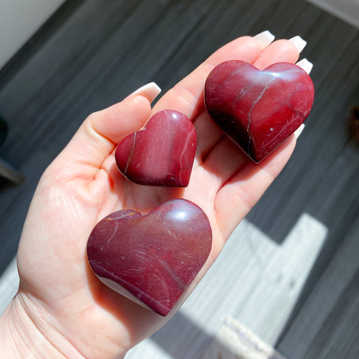 Three heart-shaped red stones held in a hand with a blurred background