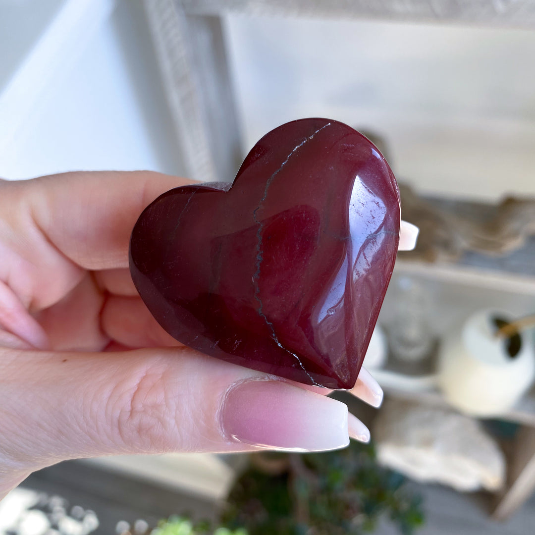 Heart-shaped red stone held in a hand with a blurred background