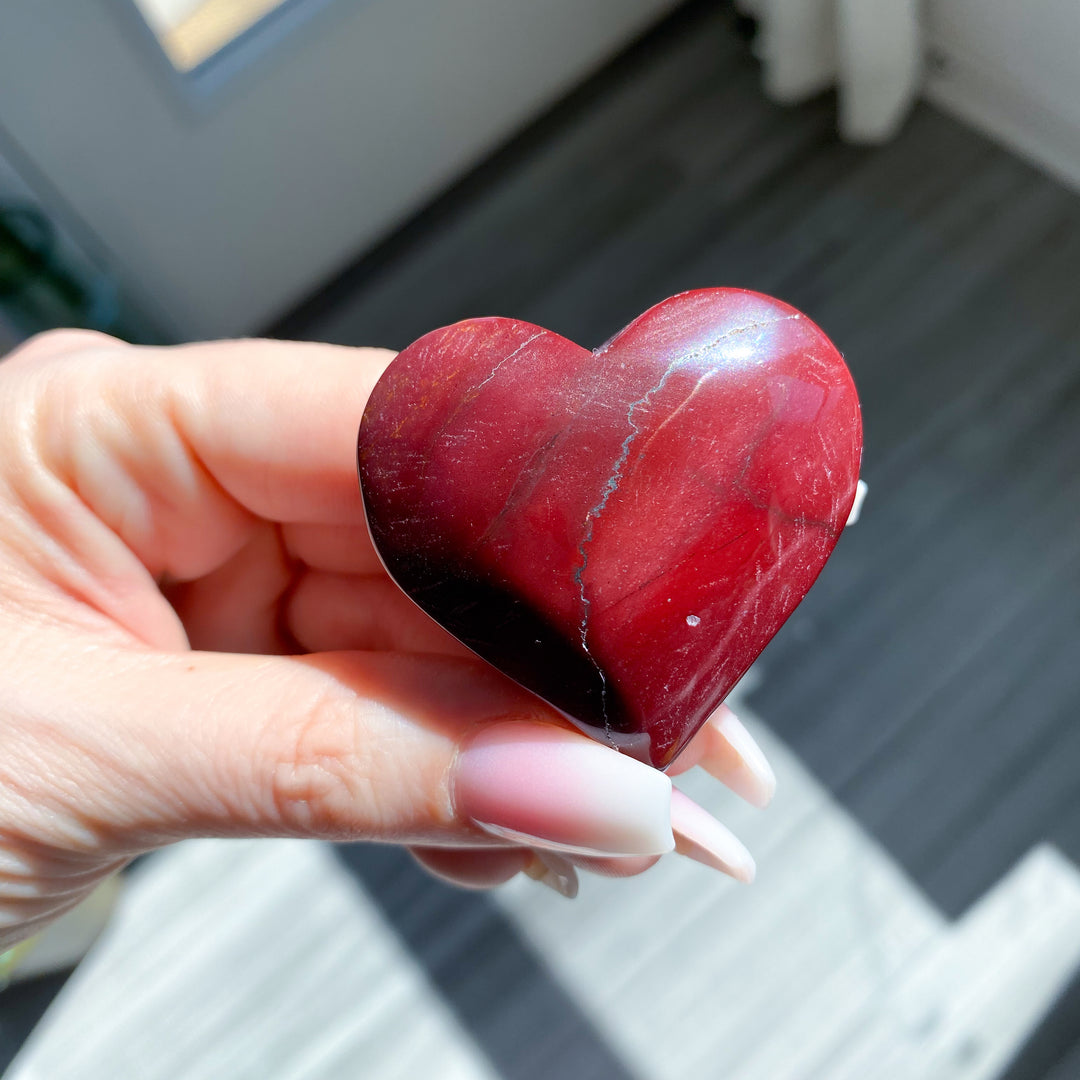 Heart-shaped red stone held in a hand with a blurred background