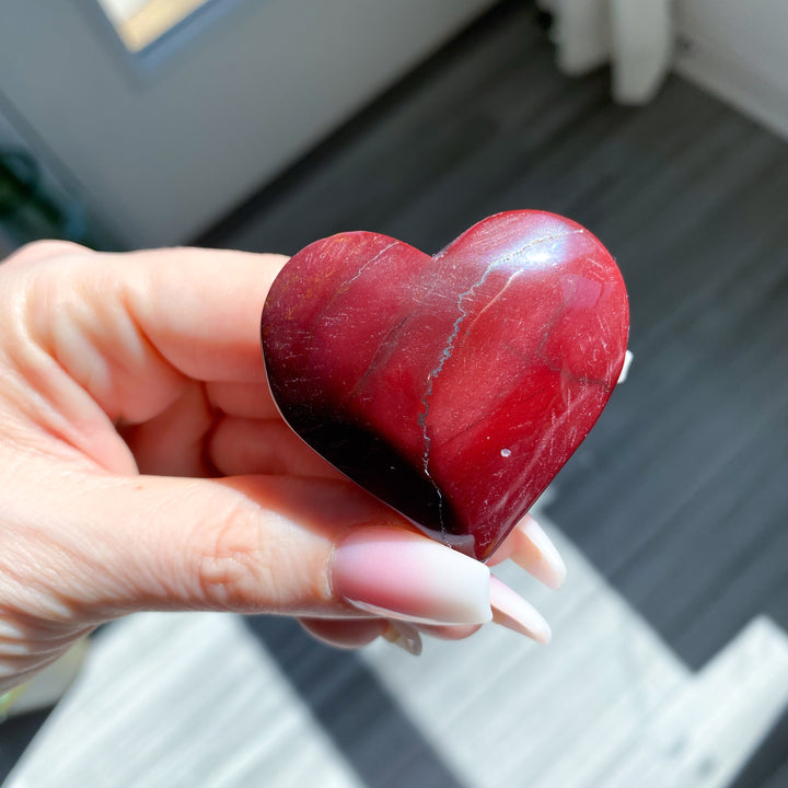 Heart-shaped red stone held in a hand with a blurred background