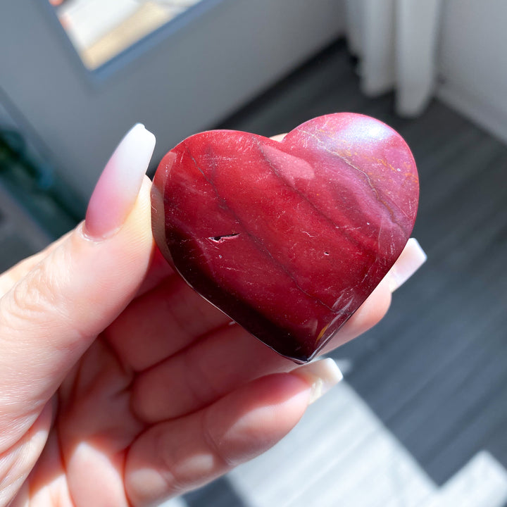 Heart-shaped red stone held in a hand with a blurred background