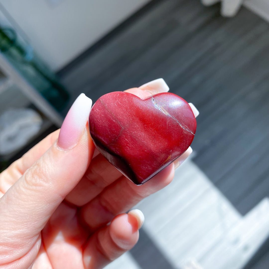 Heart-shaped red stone held in a hand with blurred background