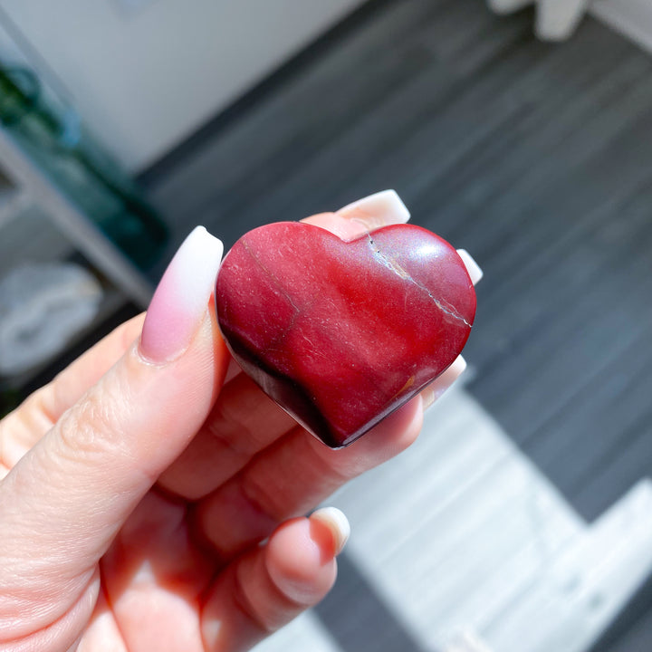 Heart-shaped red stone held in a hand with blurred background