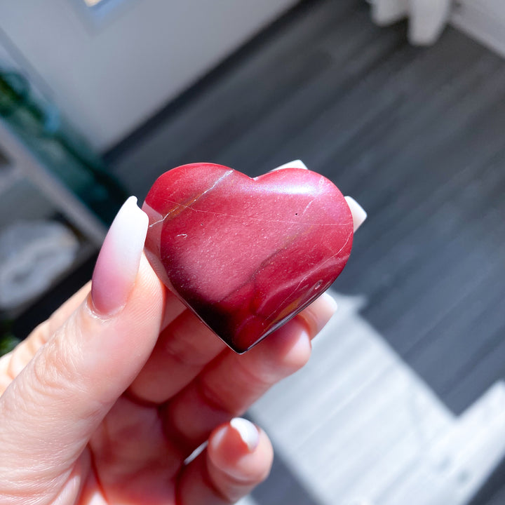 Heart-shaped red stone held in a hand with a blurred background