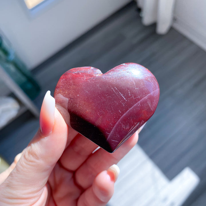 Heart-shaped red stone held in a hand with a blurred background