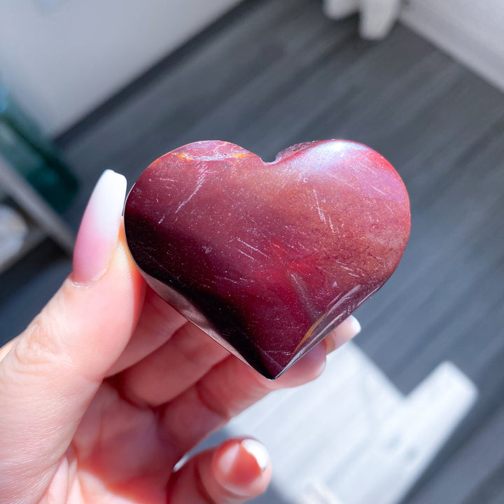 Heart-shaped red stone held in a hand with a blurred background