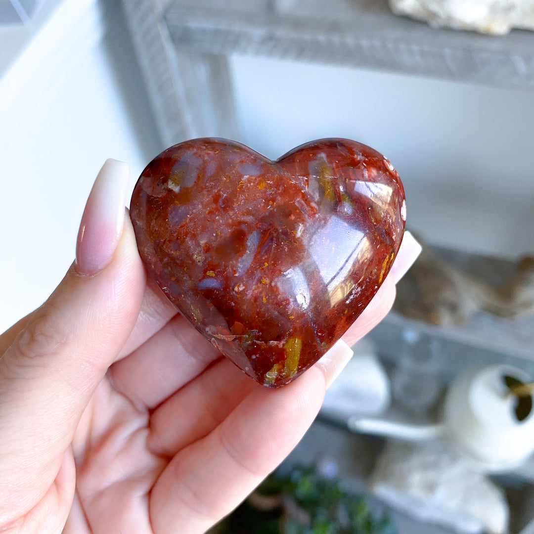 Heart-shaped red stone held in a hand with a blurred background