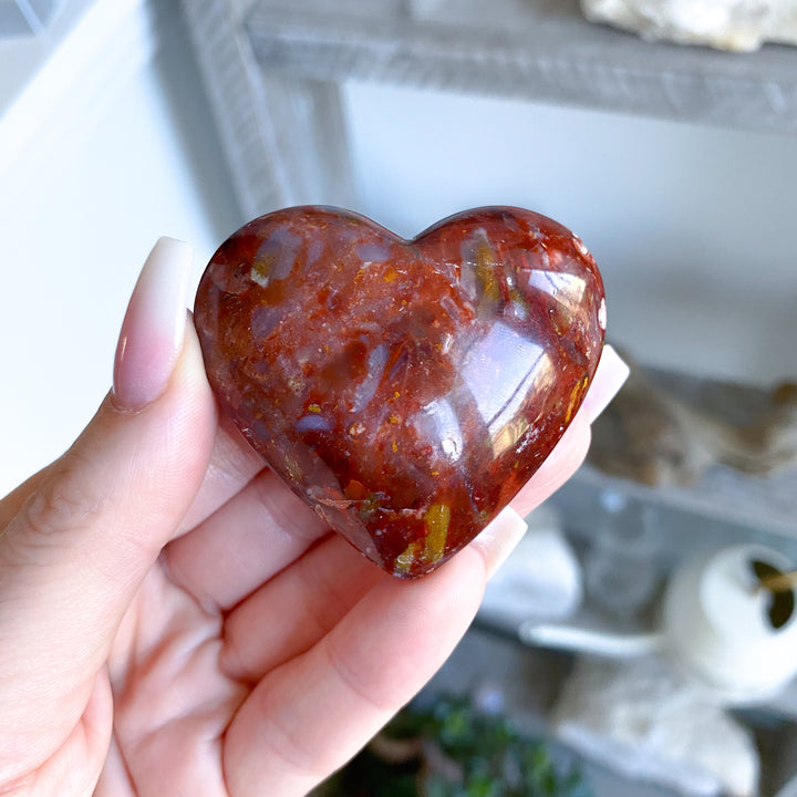 Heart-shaped red stone held in a hand with a blurred background