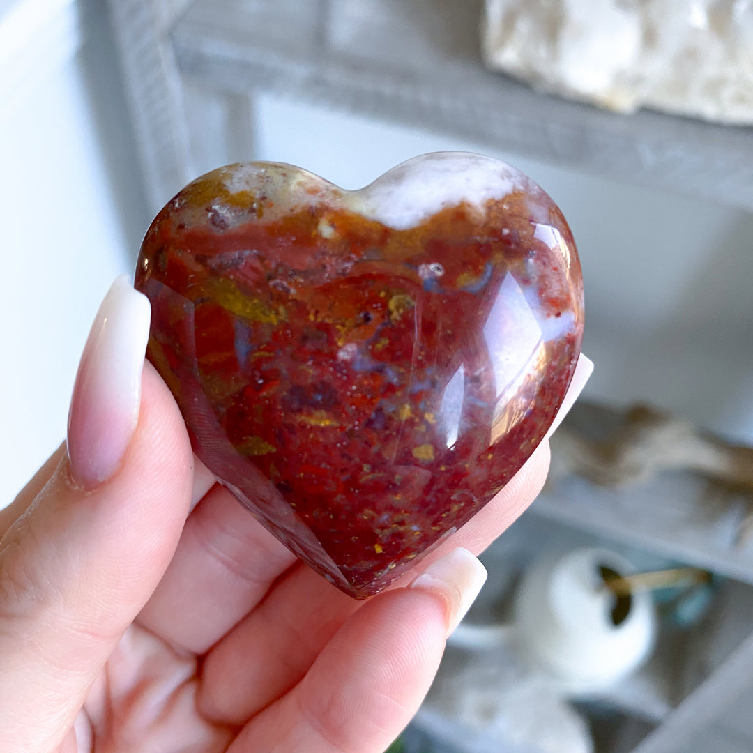 Heart-shaped red stone held in a hand with a blurred background