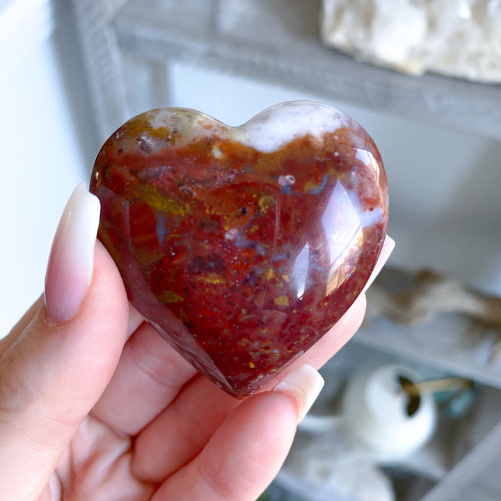 Heart-shaped red stone held in a hand with a blurred background