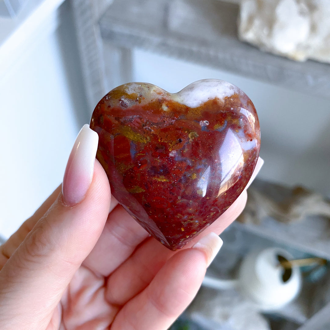 Heart-shaped red stone held in a hand with a blurred background